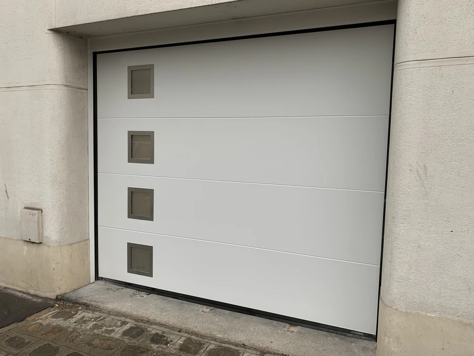 Porte de garage sectionnelle blanche moderne installée dans une façade de bâtiment aux murs en béton brut