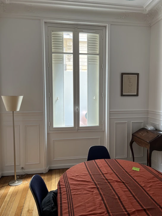 Intérieur de bureaux classiques aux murs blancs et boiseries, avec portes-fenêtres à petits carreaux donnant sur la rue