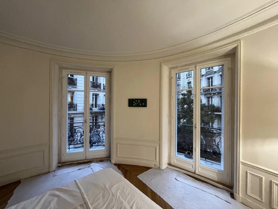 Intérieur d'un appartement haussmannien parisien avec deux portes-fenêtres blanches donnant sur des balcons avec balustrades en fer forgé