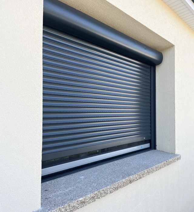Volet roulant aluminium bleu et gris installé sur façade extérieure blanche
