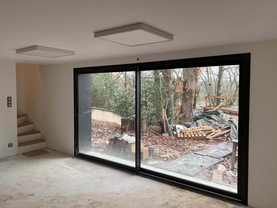 Intérieur en cours de finition avec baie vitrée coulissante à double vantaux en aluminium noir donnant sur terrasse extérieure
