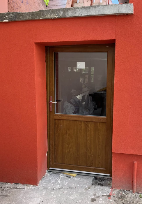 Porte d'entrée en bois marron avec vitrage supérieur, intégrée dans une façade extérieure peinte en rouge vif