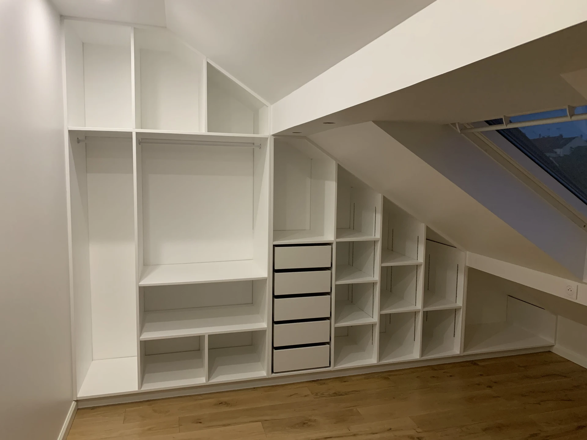 Intérieur d'un dressing sous combles aménagé avec un système de rangement modulaire blanc