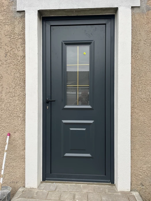 Porte d'entrée résidentielle en aluminium anthracite, encadrement blanc sur façade pierre de taille beige