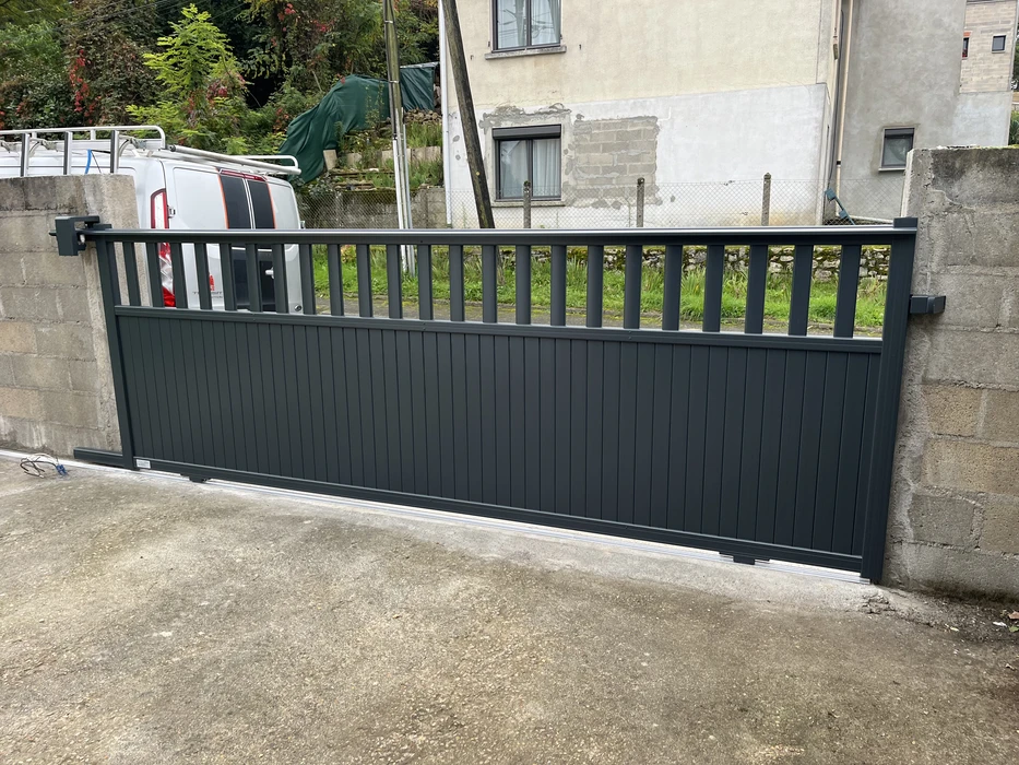 Portail d'entrée coulissant en aluminium anthracite, installé sur allée bétonnée entre piliers en maçonnerie