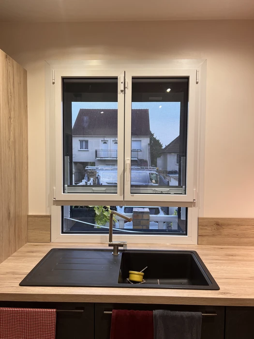 Intérieur moderne avec fenêtre triple vitrage à menuiserie blanche et cadre noir, donnant sur rue résidentielle
