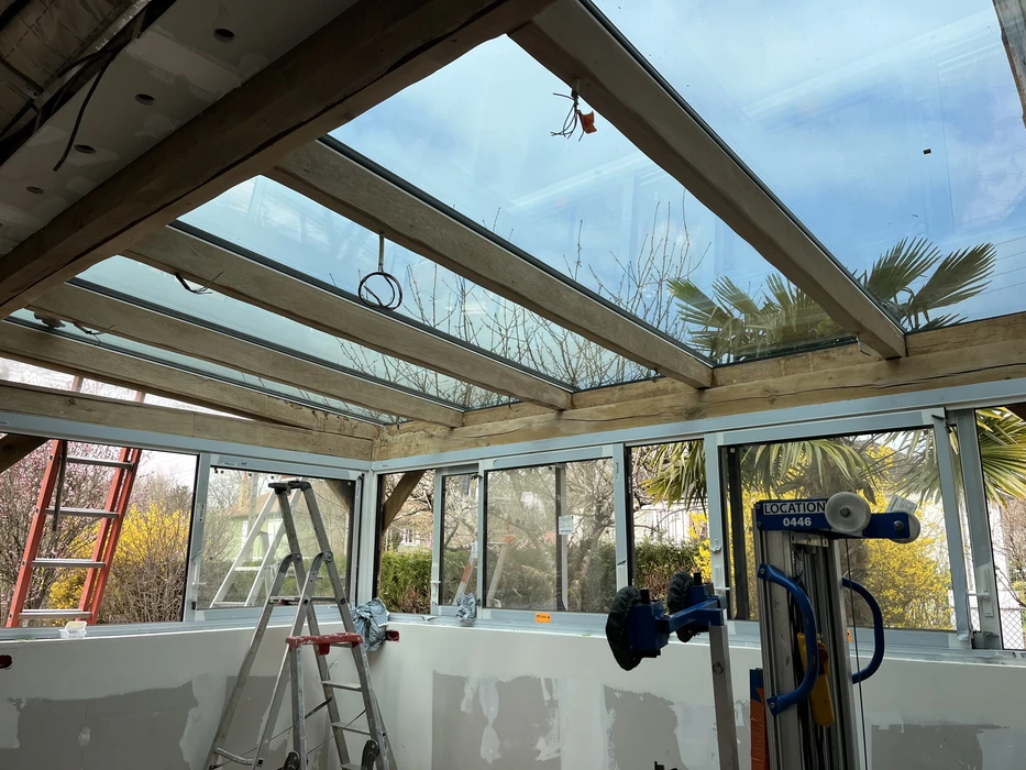Véranda en construction avec structure en bois clair et baies vitrées couleur bleu ciel