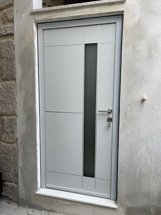 Entrée extérieure avec portes battantes en aluminium anthracite à trois vantaux, montées sur façade enduite beige