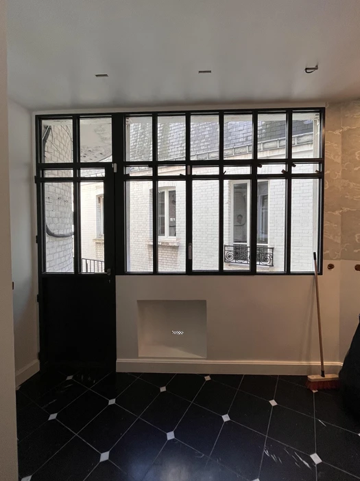 Intérieur d'un espace en rénovation avec verrière panoramique à structure métallique noire et vitrage transparent offrant vue sur ciel bleu