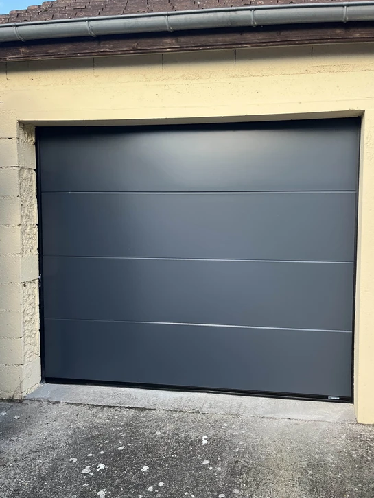 Intérieur résidentiel moderne présentant une porte vitrée coulissante de style atelier avec cadre noir et panneaux opaques inférieurs, installée dans un couloir carrelé blanc